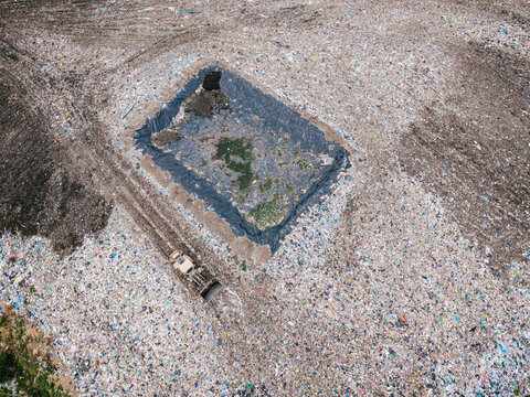 Aerial view of a municipal solid waste landfill with a large lined leachate collection pond and a bulldozer working on the waste pile in Laidzes pagasts, Talsu novads, Latvia.