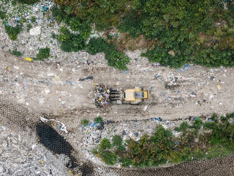 Aerial view of a bulldozer moving waste at a municipal solid waste landfill, with piles of trash, sorted materials, and surrounding greenery in Laidzes pagasts, Talsu novads, Latvia.