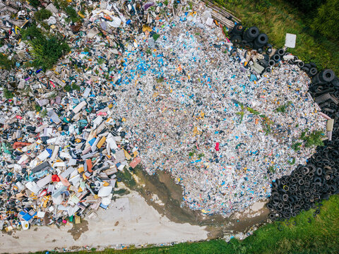 Aerial view of a large landfill site filled with piles of plastic waste, discarded tires, and various debris surrounded by green vegetation, Laidzes pagasts, Talsu novads, Latvia.