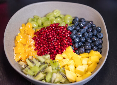 Fruit salad with kiwi, oranges, pineapple, blueberries, grapes, and pomegranate seeds in a bowl. Sweet food, healthy eating, organic, ripe, prepearing salad, ready to eat.