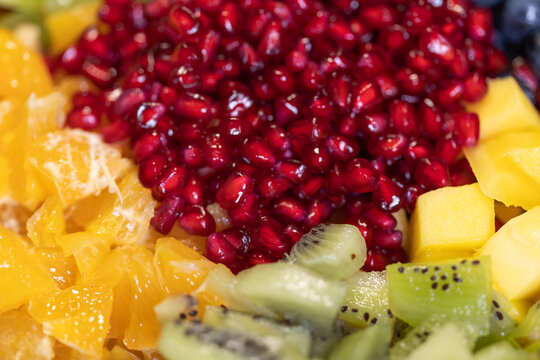 Close-up of kiwi, oranges, pineapple and pomegranate seeds in a bowl for a fruit salad. Sweet foods, healthy eating, organic, ripe, preparing a salad, ready to eat.
