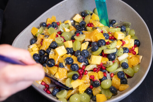 Mixed fruit salad with kiwi, oranges, pineapple, blueberries, grapes, and pomegranate seeds in a bowl. Sweet food, healthy eating, organic, ripe, prepearing salad, ready to eat.