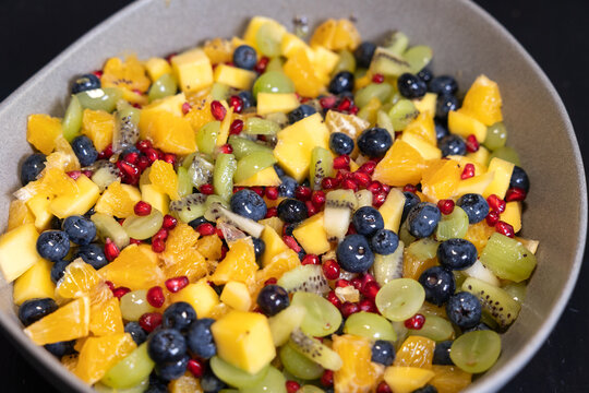 Mixed fruit salad with kiwi, oranges, pineapple, blueberries, grapes, and pomegranate seeds in a bowl. Sweet food, healthy eating, organic, ripe, prepearing salad, ready to eat.