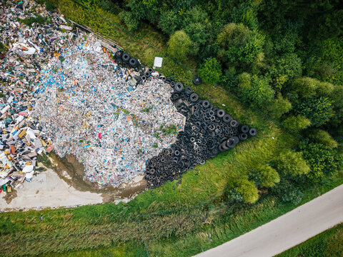 Aerial view of a large landfill site featuring a massive pile of discarded tires and mixed waste, surrounded by dense green forest and a nearby road in Laidzes pagasts, Talsu novads, Latvia.