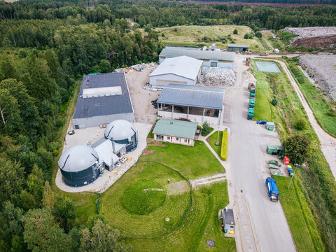 Aerial view of a municipal solid waste management facility with large storage buildings, industrial processing domes, and waste collection vehicles in Laidzes pagasts, Talsu novads, Latvia.