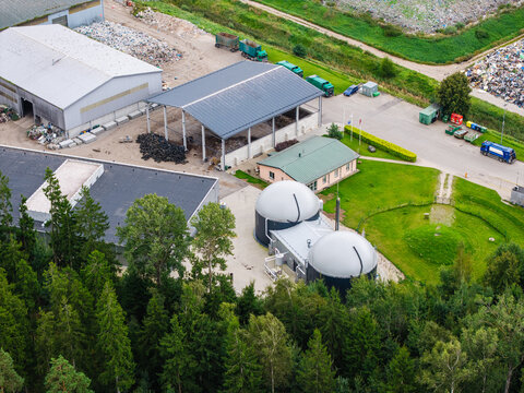 Aerial view of a municipal solid waste landfill and waste management facility with processing buildings, storage tanks, and surrounding forest in Laidzes pagasts, Talsu novads, Latvia.