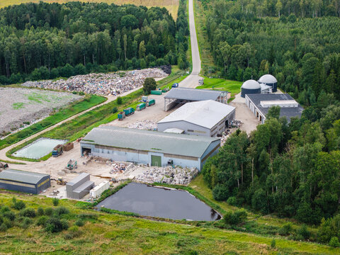Aerial view of a municipal solid waste landfill and waste management facility with processing buildings, storage areas, and surrounding forest in Laidzes pagasts, Talsu novads, Latvia.