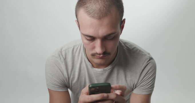 Young Man Using Smartphone and Looking at Camera on White Studio Background