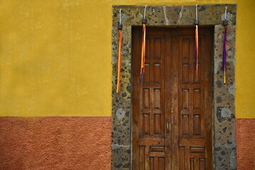 Naklejka premium Old Colonial house antique wooden door with a stone trim and satin ribbons on a two-tone stucco wall in San Miguel de Allende, Mexico.