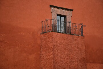 Naklejka premium Colonial house window with a stone trim and a balcony with handcrafted wrought iron railing on a Venetian red stucco wall in San Miguel de Allende, Mexico.