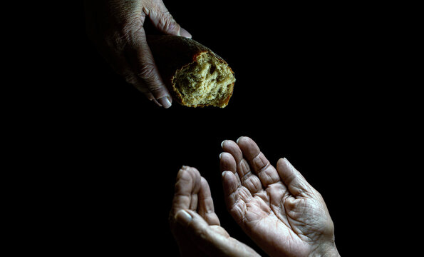 Elder woman hand give a loaf of bread to hands of a beggar. Poverty and world hunger concept. Hands grabbing for bread. Old man giving poor homeless person pieces of bread. Helping the homeless