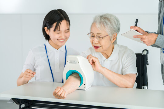 血圧計を使い血圧測定をするシニア女性と記録をとる看護師,介護士の女性スタッフ