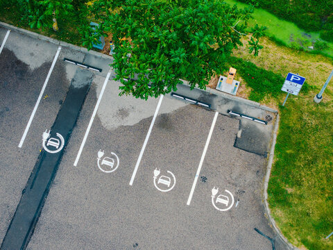 Aerial view of electric vehicle charging parking spaces with painted symbols on asphalt and adjacent green grass in Jurmala, Latvia.