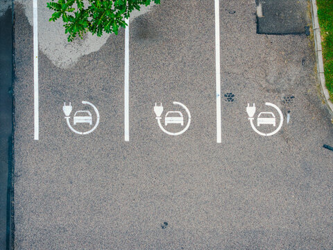 Aerial view of three electric vehicle charging station symbols painted on an asphalt parking lot in Jurmala, Latvia.