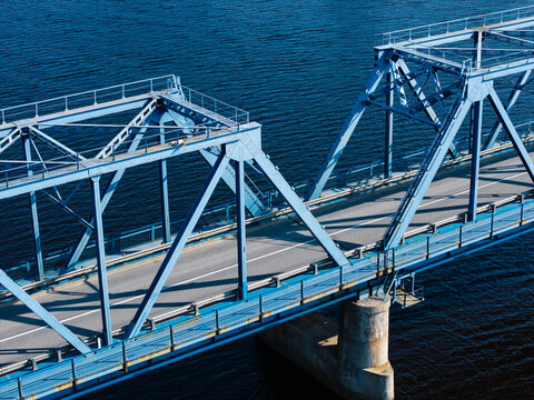 Aerial view of Kalnciema tilts, a blue steel truss bridge spanning over dark water with clear structural details and road markings, Tireli, Jelgavas novads, Latvia.