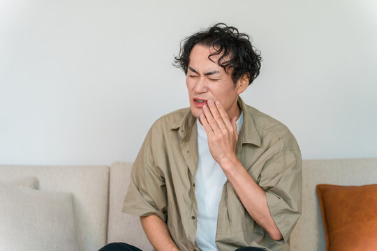 A man clutching his cheek in pain from a toothache; an image of cavities or dental problems.