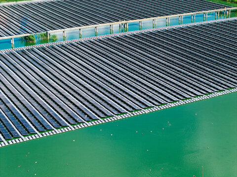 Aerial view of a floating solar power plant with rows of photovoltaic panels on green water and maintenance walkways in Jurmala, Latvia.