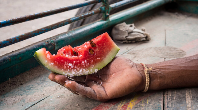 Weathered Hand Holding Fresh Watermelon Slice Sprinkled with Coarse Salt on Rustic Cart Bed