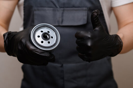Auto mechanic hand in black glove holding oil filter showing thumbs up close up, car service worker in uniform, quality vehicle repair concept, quality assurance, professional car maintenance service.