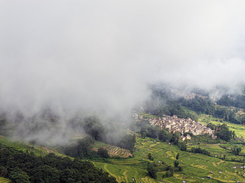 Aerial view of Yuanyang rice terraces with lush tiered fields, village houses, and clouds rolling over the mountainside in Honghe Hani and Yi Autonomous Prefecture, Yunnan, China.