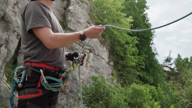 4K close up of a climber belaying his partner with a belay device on a harness at an outdoor cliff site. Rock climbing safety gear, rope management, and extreme sport concept