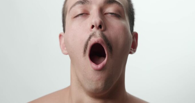 Studio Close-Up Portrait of Tired Young Caucasian Man Yawning Open Mouth