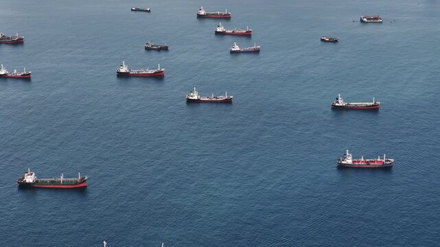 Fleet of oil tanker ships and commercial cargo vessels anchored in the deep blue sea near a long bridge. Global maritime logistics, international shipping trade, and energy transport.