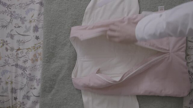 Sequence in top view: the pink children's garment is first presented closed and neatly arranged over a floral print, and then it opens gently showing its white lining and wide cut