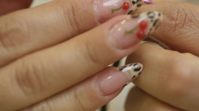 A close-up shot shows hands crocheting with dark yarn. The translucent nail polish stands out, decorated with a leather-like print and red cherry motifs with green stems