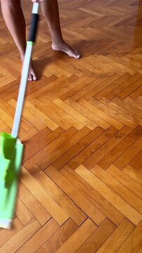 low section of man cleaning parquetry flooring with herringbone pattern inside room using microfibre pad on flat mop