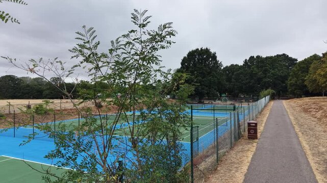 4K UHD low-altitude drone tracking shot skimming over the fully renovated public tennis courts at Raphael Park, Romford, England. Modern sports facility ready for play