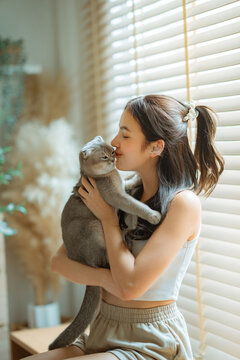 Young woman hugging and kissing her pet cat at home, affectionate bonding, love, companionship, pet care, friendship, comfort and happy lifestyle with domestic animal in cozy interior