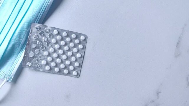 Woman's hand places a blister pack of pills on a table beside a medical face mask, medication and healthcare concept.