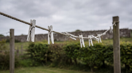 Fototapeta premium White wooden clothespins hanging on a clothesline in a rustic outdoor setting with overcast sky