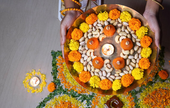 Close up of Indian girl holding hand flower plate for Diwali celebration by looking at camera at home concept of - Indian traditional, ceremony and festival preparation.