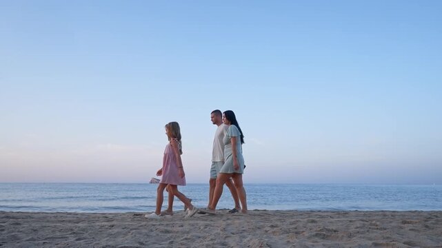 Three friends stroll along the sandy beach near the water as the sun sets in the background. They enjoy their time by the ocean and create memories together.