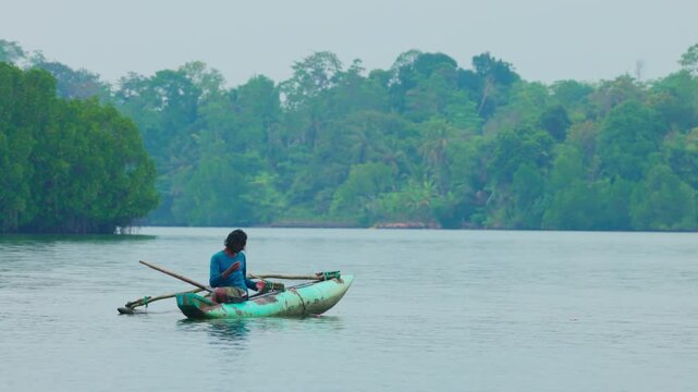 A local fisherman in a traditional Sri Lankan outrigger dugout boat (oruwa) navigates the calm waters of a body of water in Sri Lanka. fisherman swims in slow motion video. 10.02.2022 SRI LANKA.