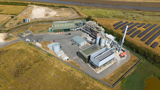 Aerial view of a biomass energy power plant with industrial infrastructure, storage tanks, and adjacent solar panel arrays in a rural landscape in Boston, England, United Kingdom.