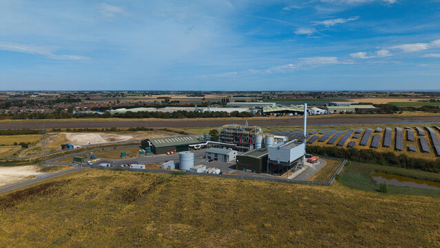 Aerial view of a biomass energy power plant featuring industrial buildings, storage tanks, and adjacent solar panel arrays set within a rural landscape in Boston, England, United Kingdom.
