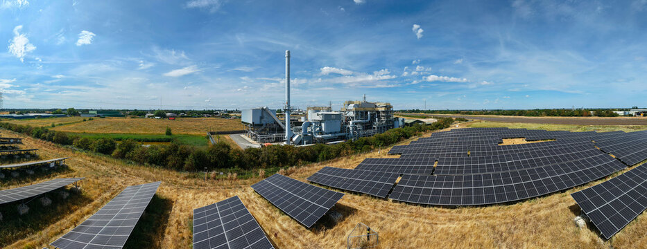 Aerial view of a biomass energy power plant surrounded by extensive solar farms with rows of photovoltaic panels in the rural landscape of Boston, England, United Kingdom.
