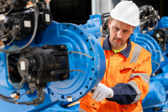 Engineer inspecting industrial robotic arm and machinery in factory, technician maintaining automated equipment in manufacturing plant, industrial worker checking machinery parts in factory warehouse
