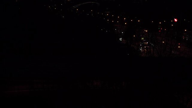 Night aerial view of city lights and public train commuting through dark urban area.