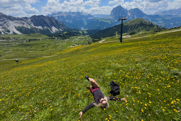 Naklejka premium Young woman lies relaxed on grass in a mountain meadow wearing casual clothes enjoying nature and tranquility on a sunny day. 