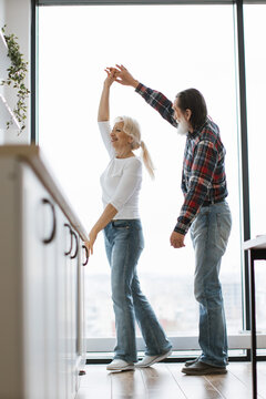 A happy senior couple enjoys a spontaneous dance together by a large window, celebrating their enduring love and connection