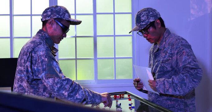 Two uniformed soldiers play foosball indoors under blue light, creating a casual moment of teamwork, recreation and stress relief.