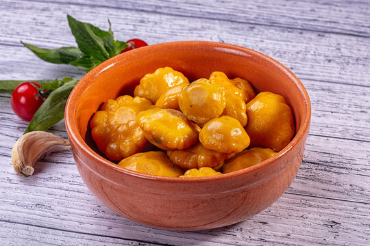 Pickled yellow patisson squash in terracotta bowl with fresh garlic and tomatoes on rustic wooden table