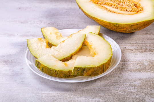 Sliced piel de sapo melon on white plate with half melon in background