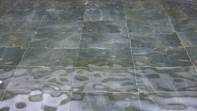 Close-up of clear moving water with ripples and reflections over green tiles in pool during daytime