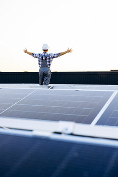 Engineer standing on rooftop solar power station, arms outstretched, celebrating sustainable renewable energy success