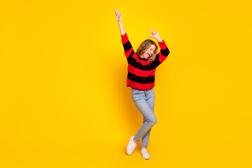 Cheerful young woman in a colorful striped sweater posing joyfully on a vibrant yellow background...